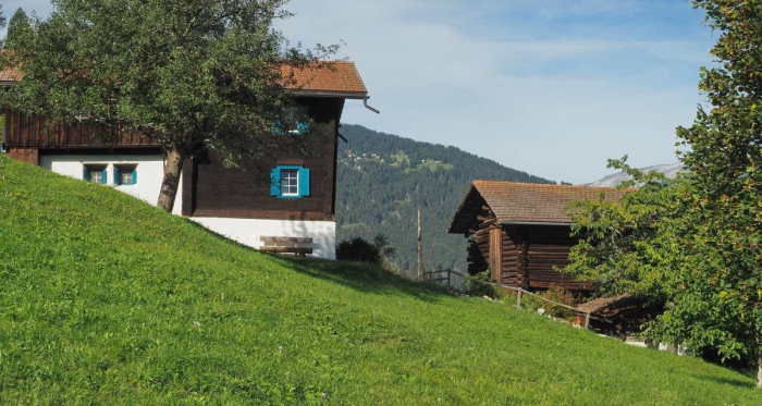 Vorbei an den sonnengebräunten Holzhäuser von Praden